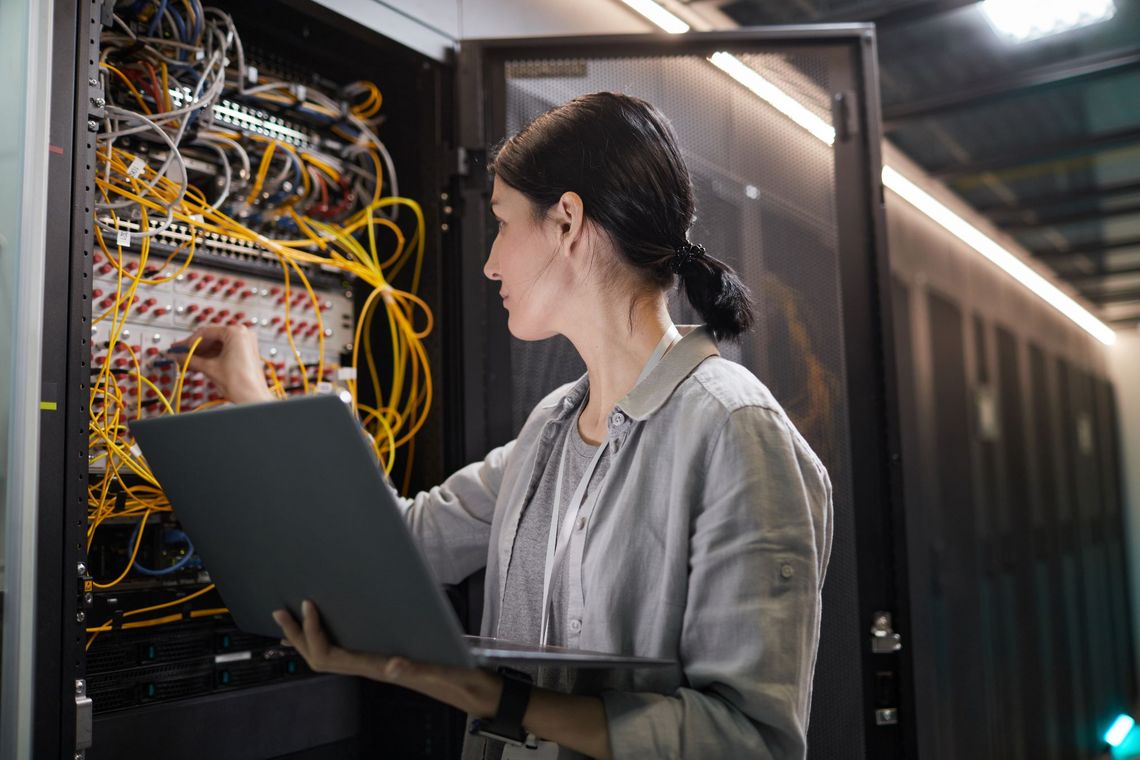 Frau mit Laptop vor einem Serverschrank