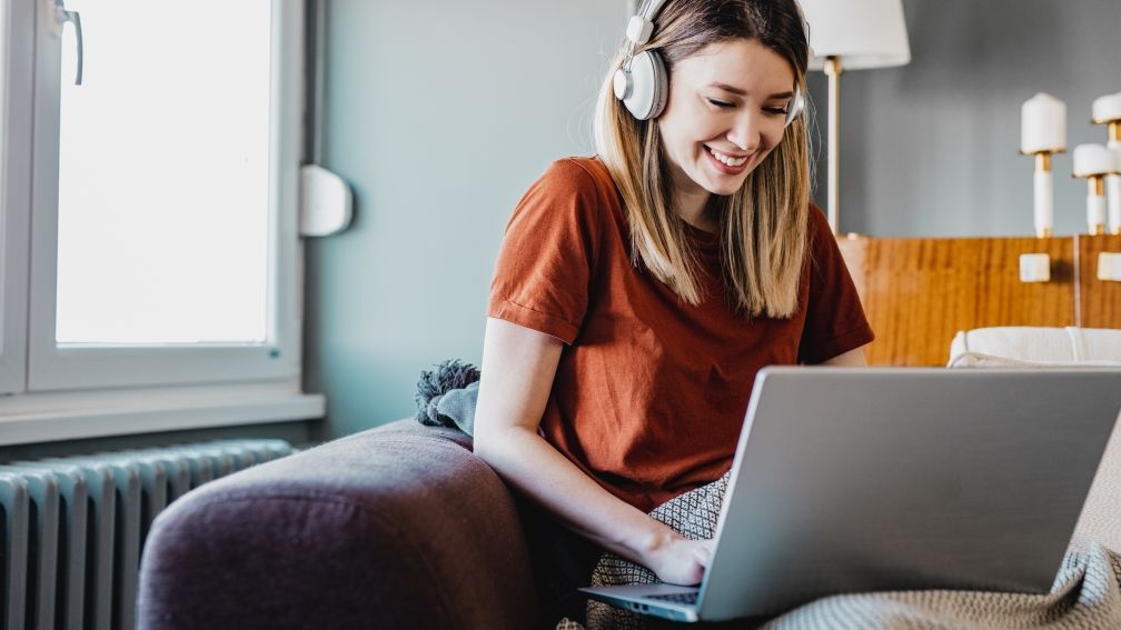 Frau mit Kopfhörern und Laptop auf dem Sofa sitzend