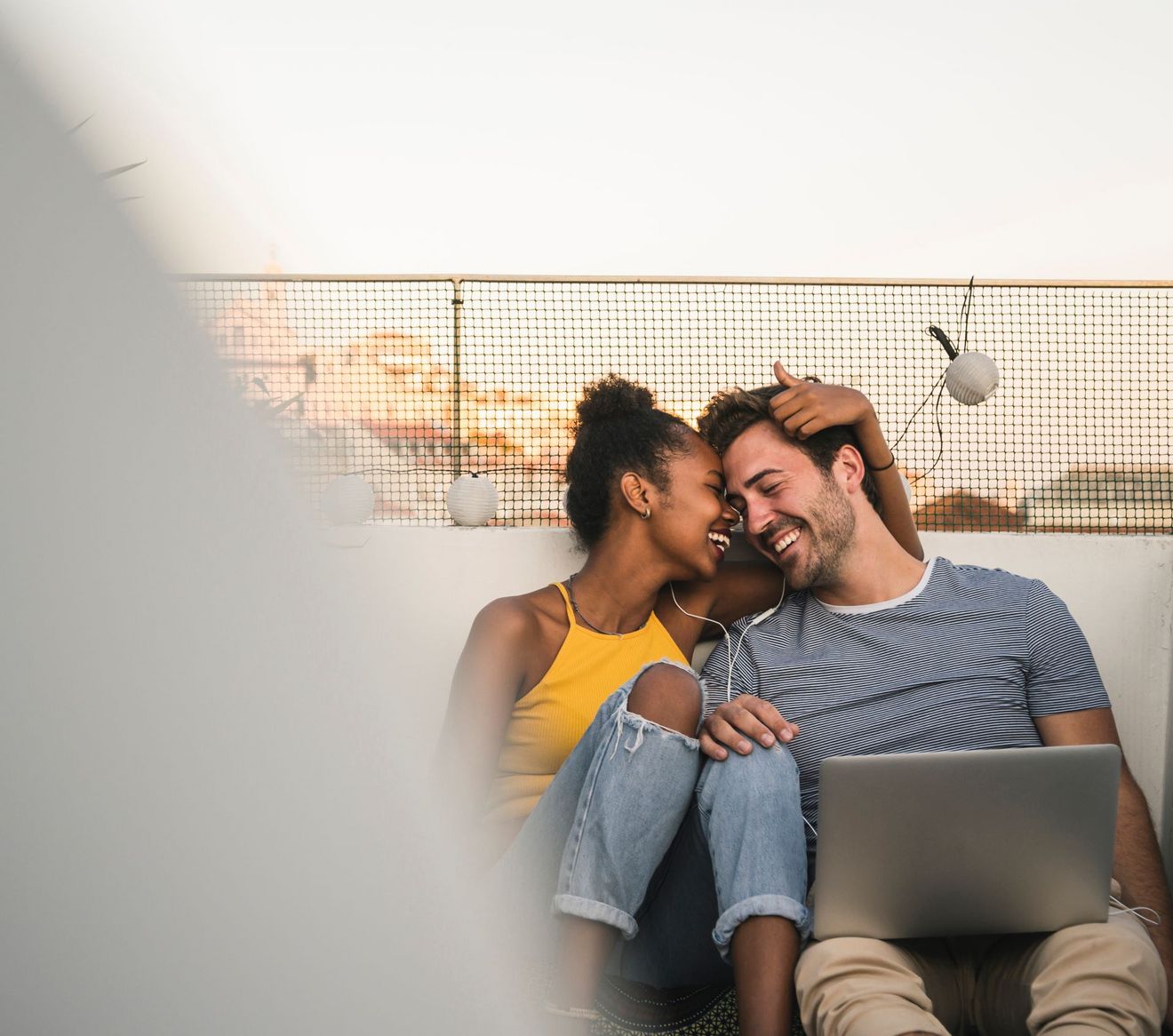 Ein Mann und eine Frau sitzen auf einer Dachterrasse mit einem Laptop.