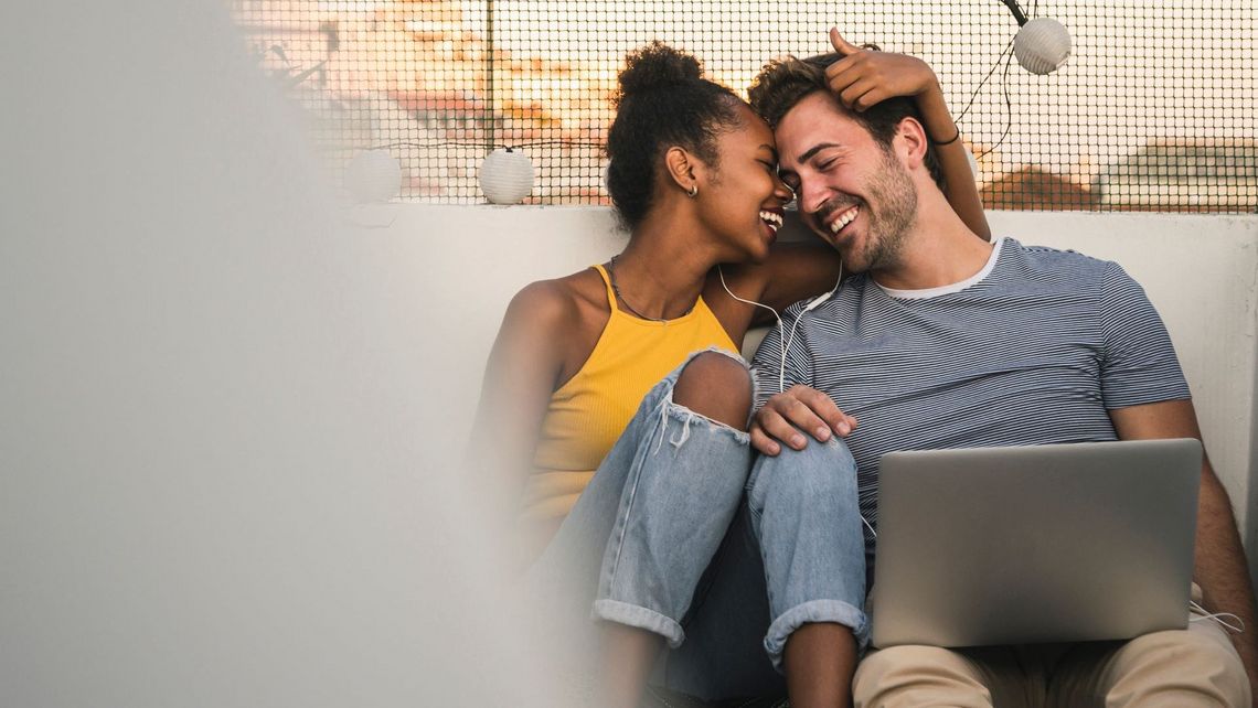 Ein Mann und eine Frau sitzen auf einer Dachterrasse mit einem Laptop.