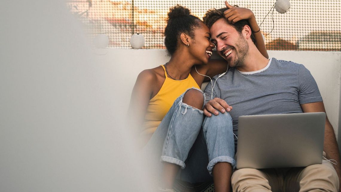 Ein Mann und eine Frau sitzen auf einer Dachterrasse mit einem Laptop.