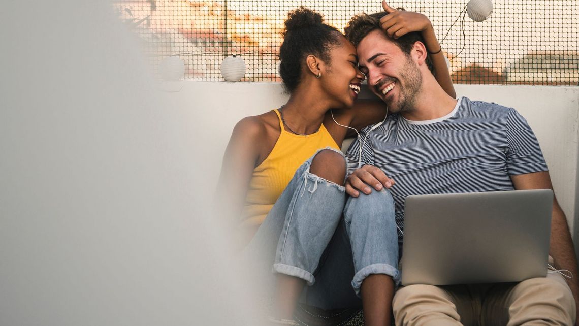 Ein Mann und eine Frau sitzen auf einer Dachterrasse mit einem Laptop.