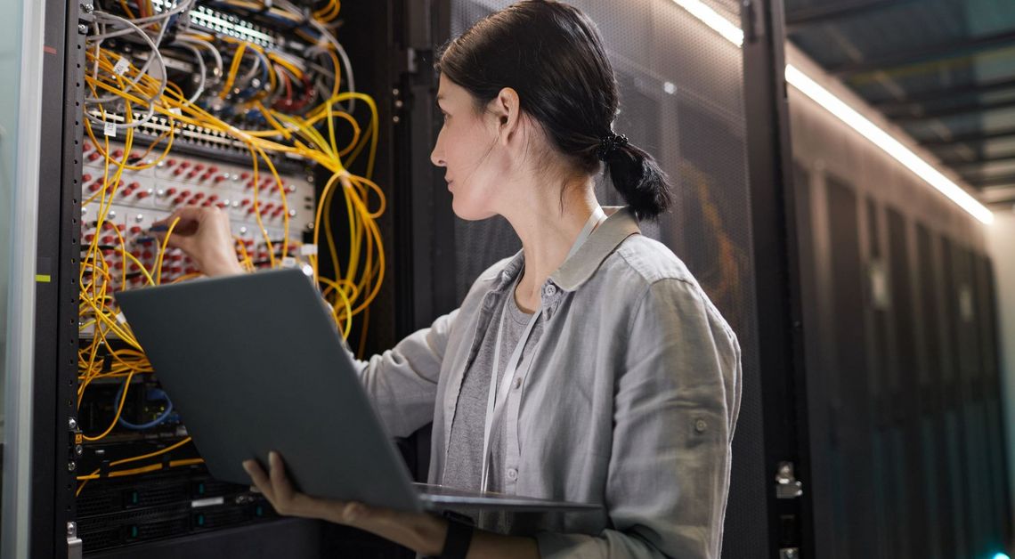 Frau mit Laptop vor einem Serverschrank