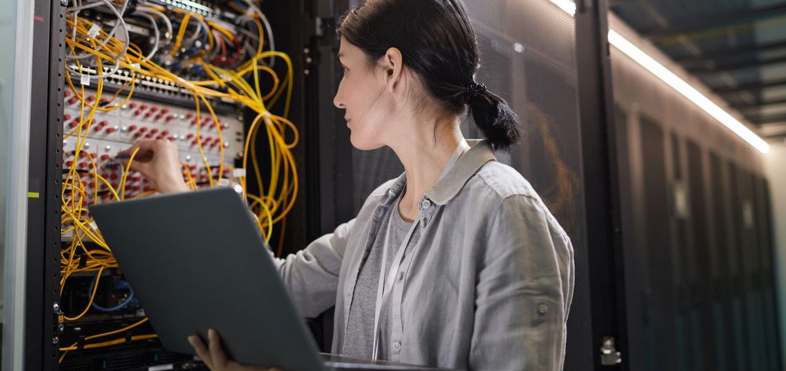 Frau mit Laptop vor einem Serverschrank