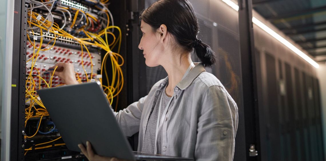 Frau mit Laptop vor einem Serverschrank