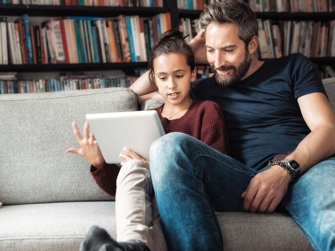 Vater mit Tochter auf dem Sofa sitzend am Laptop