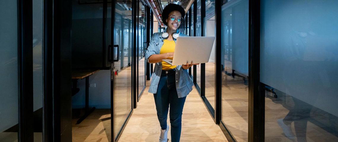 Frau läuft mit Laptop durch Büroflur
