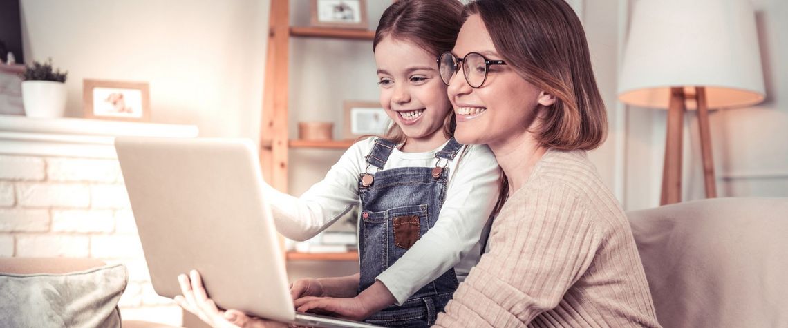 Frau mit Tochter im Wohnzimmer vor dem Laptop sitzend