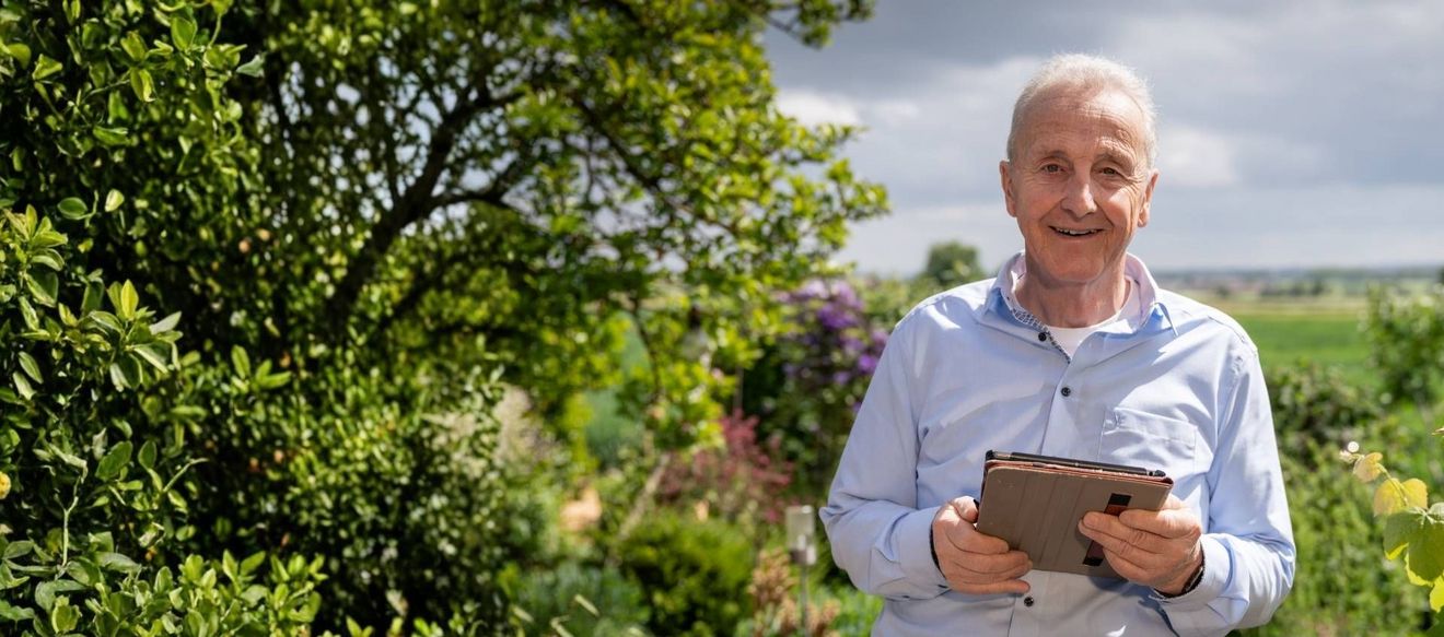 älterer Herr mit Tablet in der Hand im Garten