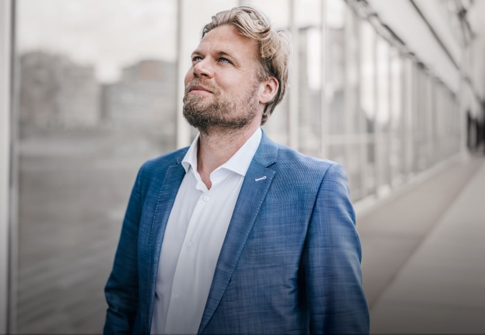 Mann mit blauem Sakko, stehend vor einem Firmengebäude